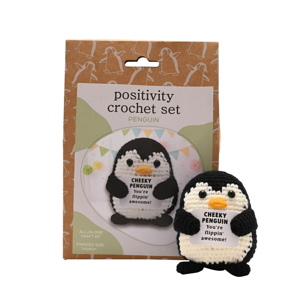 Positivity Crochet Set Penguin, featuring a finished black and white crocheted penguin with a yellow beak in the foreground, next to its brown cardboard packaging box.