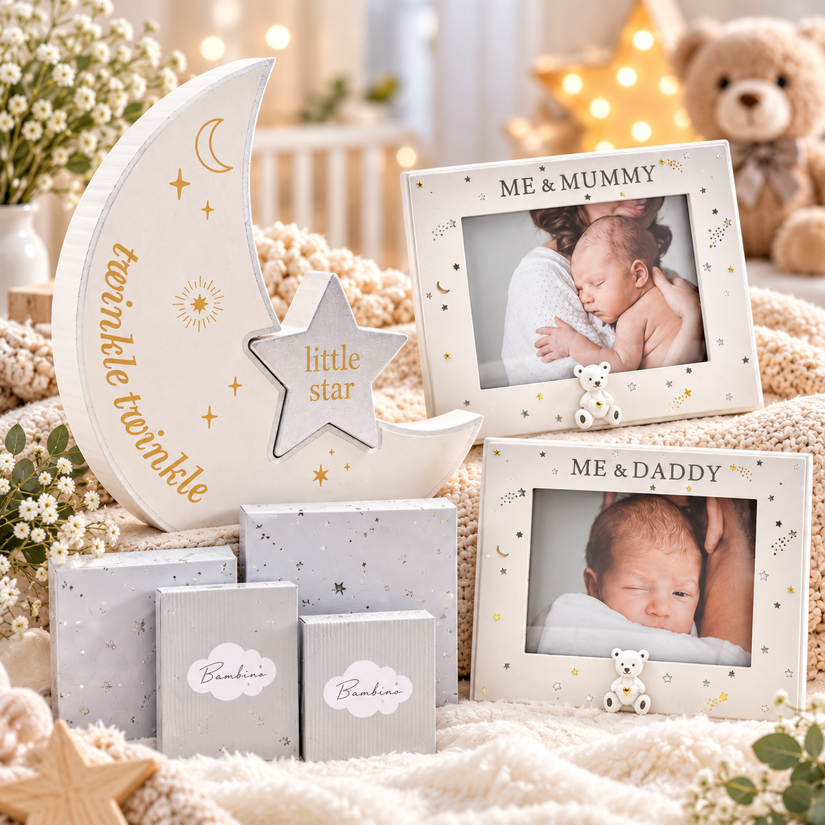 A styled baby photo frame set displayed on a soft cream blanket with decorative props. The set includes a large crescent moon frame with gold stars and the words 'twinkle twinkle little star,' a small star frame, two square photo frames labeled 'ME & MUMMY' and 'ME & DADDY' with baby photos, three small boxes labeled 'Bebine!,' and wrapped gift boxes.