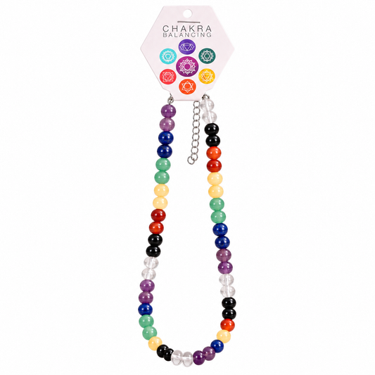 A chakra balancing beaded necklace with seven distinct colored beads representing the chakras, hanging from a pink hexagonal card labeled 'CHAKRA BALANCING' on a white background.