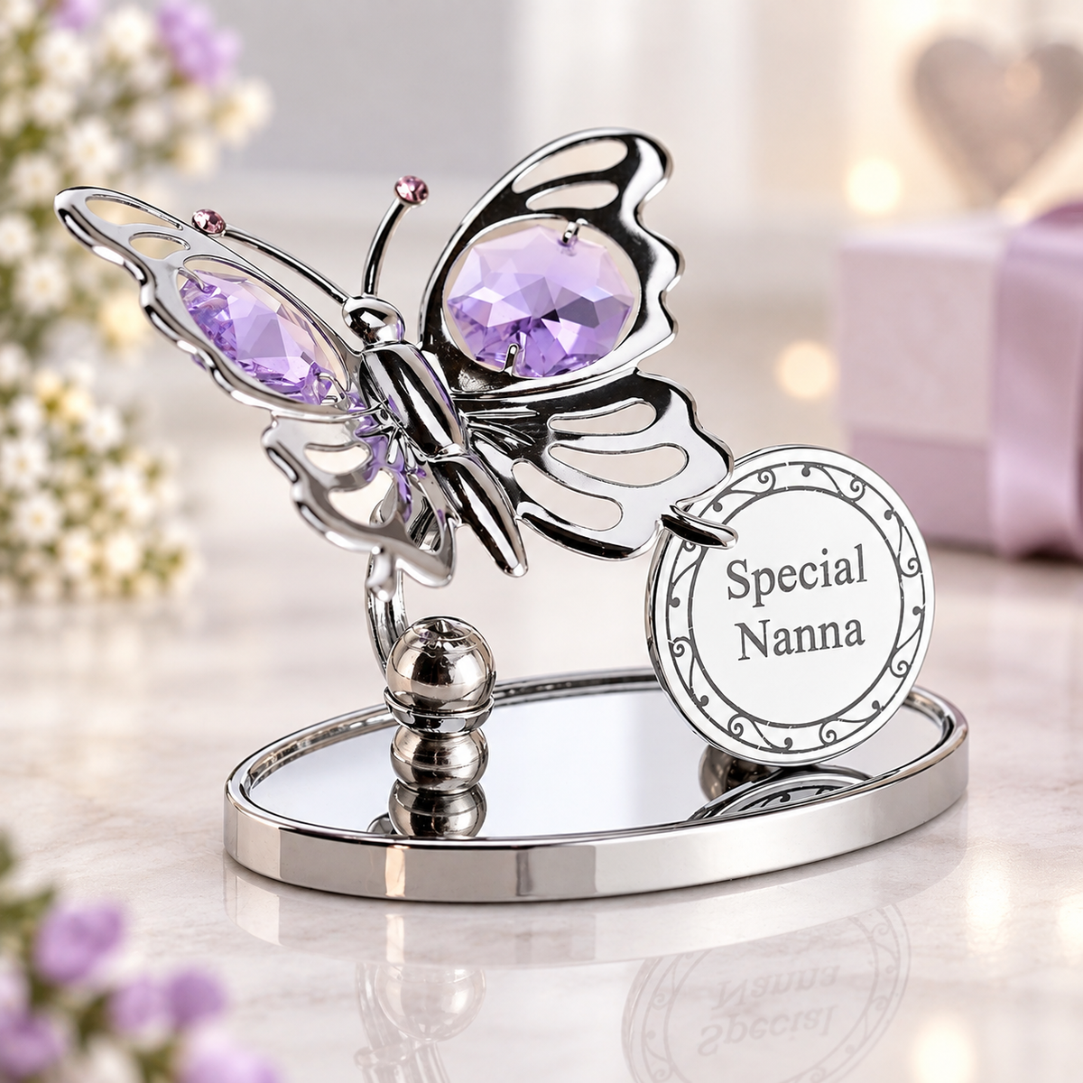 A silver butterfly-shaped keepsake holder with large purple faceted gemstones in its wings, mounted on a mirrored oval base. A round hanging tag reads 'Special Nanna.