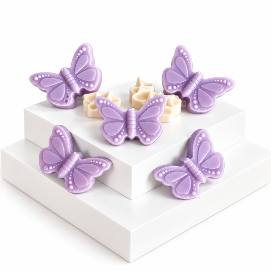 Five lavender butterfly-shaped Wax melts arranged on white display blocks, with a few pale cream star-shaped items nestled behind them, photographed on a clean white background.