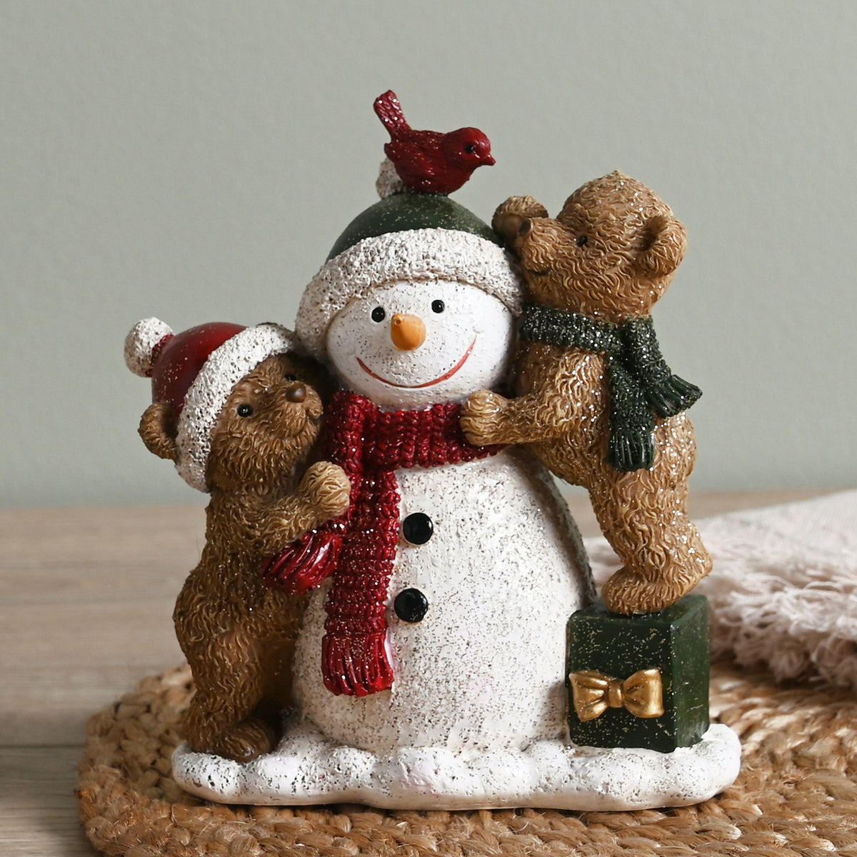 Decorative figurine of a snowman with two bears and a cardinal on a textured surface.