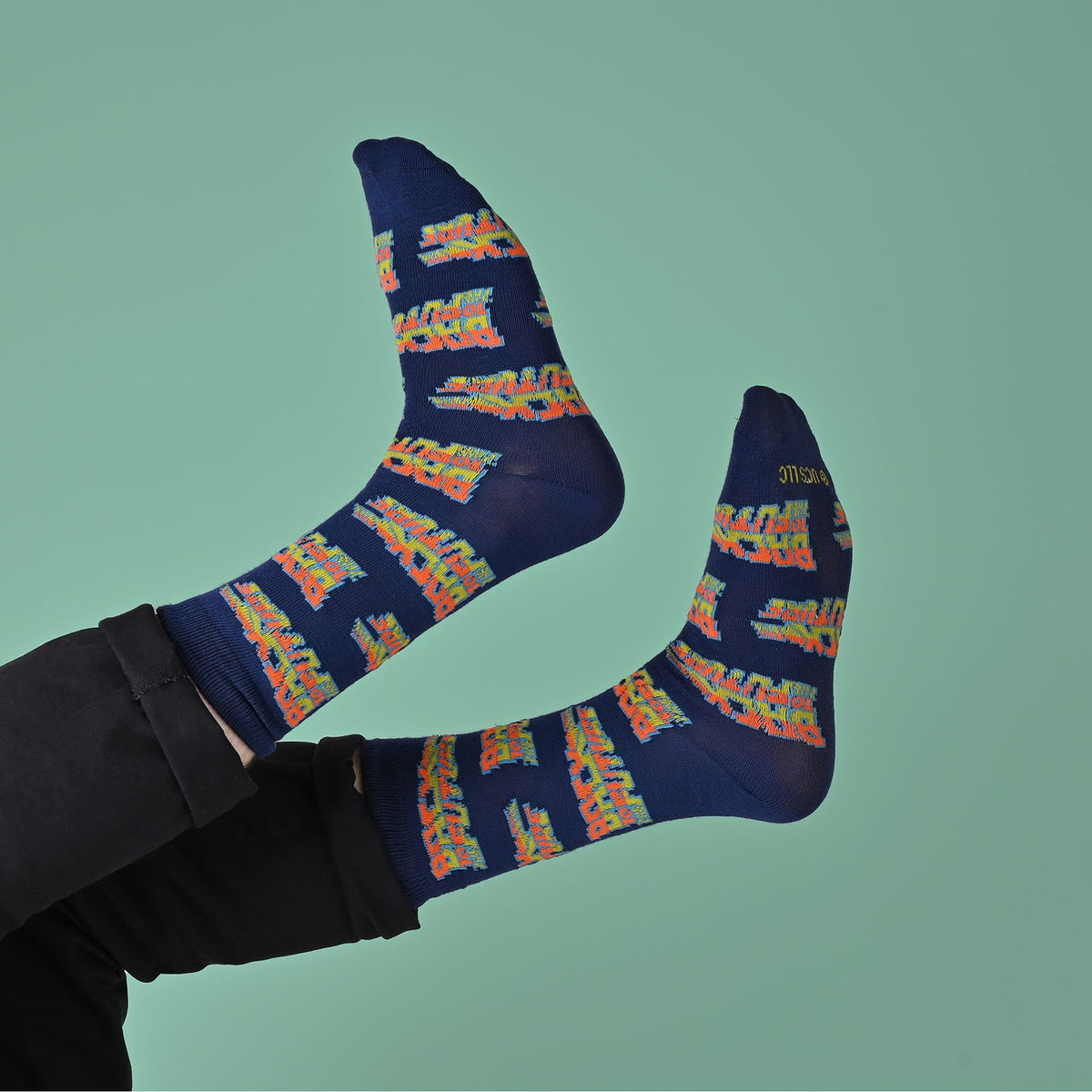 a persons legs in the air wearing navy blue socks with a colorful 'Back to the Future' on a pale green background