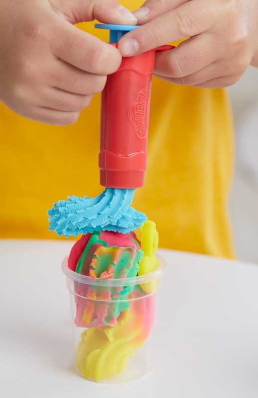 Colorful toy with a pump and colorful ball inside a clear cup, held by hands against a yellow background.