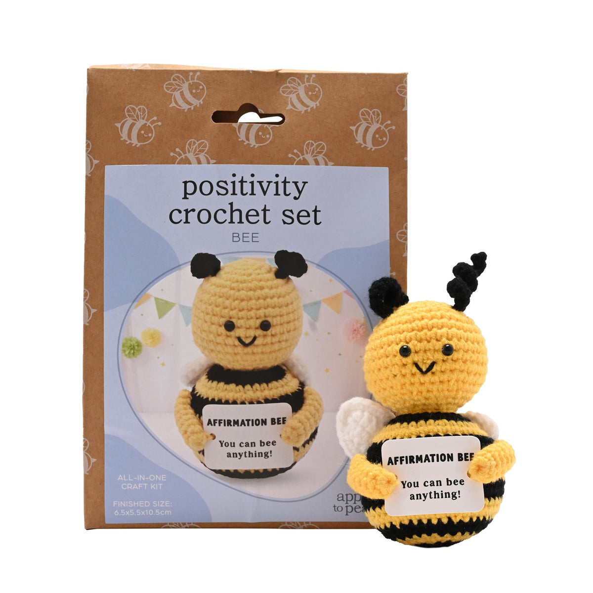 A crocheted bee affirmation set shown with its retail packaging. The set includes a yellow and black crocheted bee holding a sign that says 'AFFIRMATION BEE You can bee anything!' alongside its brown cardboard box labeled 'positivity crochet set BEE'.