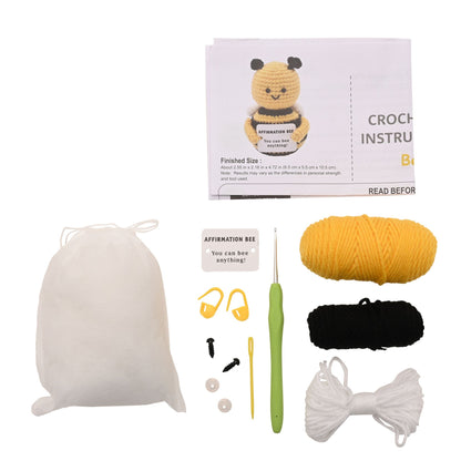 Crochet bee affirmation set kit with a white drawstring bag, crochet hook, yellow and black yarn, white thread, stitch markers, needles, and an instruction booklet featuring a crocheted bee.