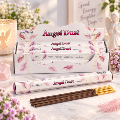A display box and individual package of Stanford Angel Dust incense sticks, with several brown incense sticks arranged in front on a soft, decorative tabletop setting with flowers and a glowing candle.