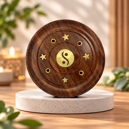 A round wooden incense burner with gold star and yin-yang details, displayed on a round stone pedestal in a warm, softly lit setting.