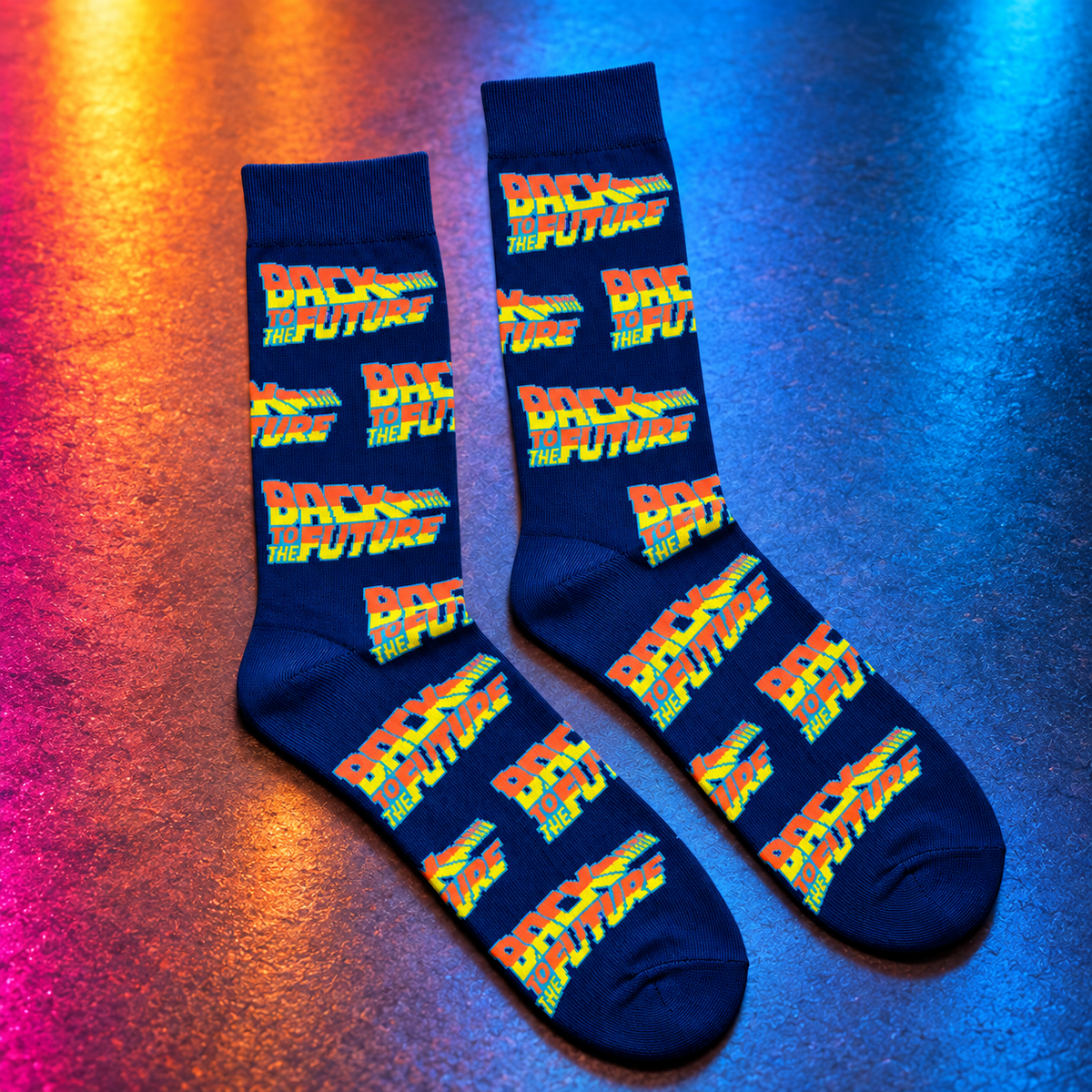 A pair of navy crew socks with a repeating 'Back to the Future' logo pattern in red, orange, yellow, and green, displayed on a textured surface with blue and orange lighting.