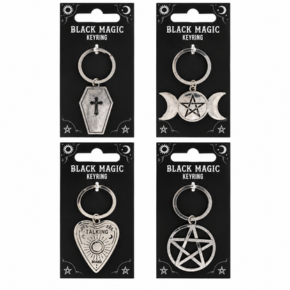 Four silver metal keyrings on black hanging cards labeled 'BLACK MAGIC KEYRING,' featuring coffin, triple moon, playing card, and pentagram designs.