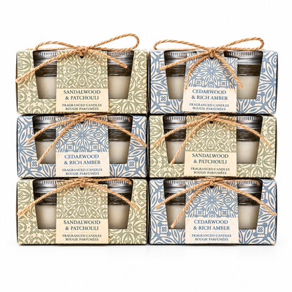 Six boxed scented candles arranged in a 3-by-2 grid on a white background. Each package contains two small glass jar candles tied with twine and a front label reading either Sandalwood & Patchouli or Cedarwood & Rich Amber.