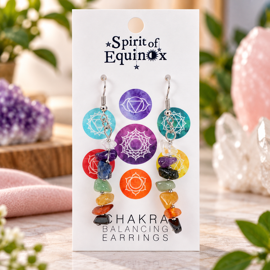 A pair of chakra balancing earrings displayed on a white card labeled 'Spirit of Equinox' and 'Chakra Balancing Earrings.' The earrings feature colorful gemstone chips in red, orange, yellow, green, blue, and purple with white chakra symbols on circular charms.