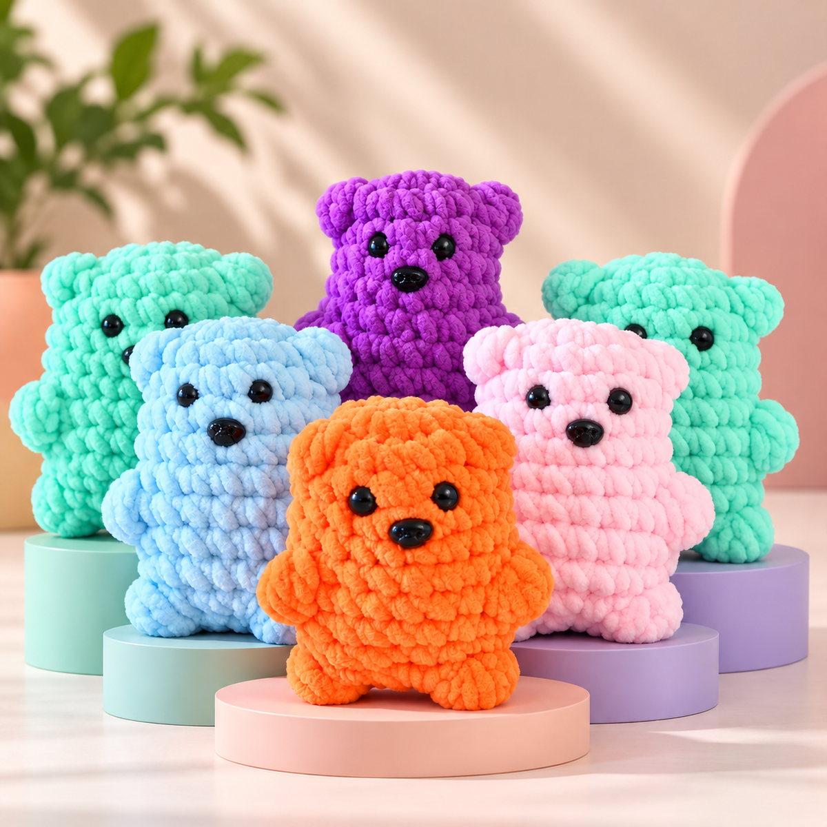 Five crocheted teddy bear toys in pastel and bright colors, including orange, pink, light blue, purple, and mint green, arranged on round display pedestals against a soft beige background.