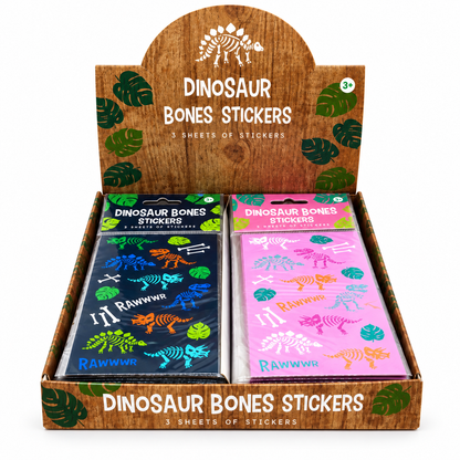 A retail display box of dinosaur bones stickers, showing two packaged sheets: one dark blue with multicolored dinosaur and bone illustrations, and one pink with colorful dinosaur and bone illustrations. The display box is wood-grain styled with green leaf prints and reads 'DINOSAUR BONES STICKERS'.