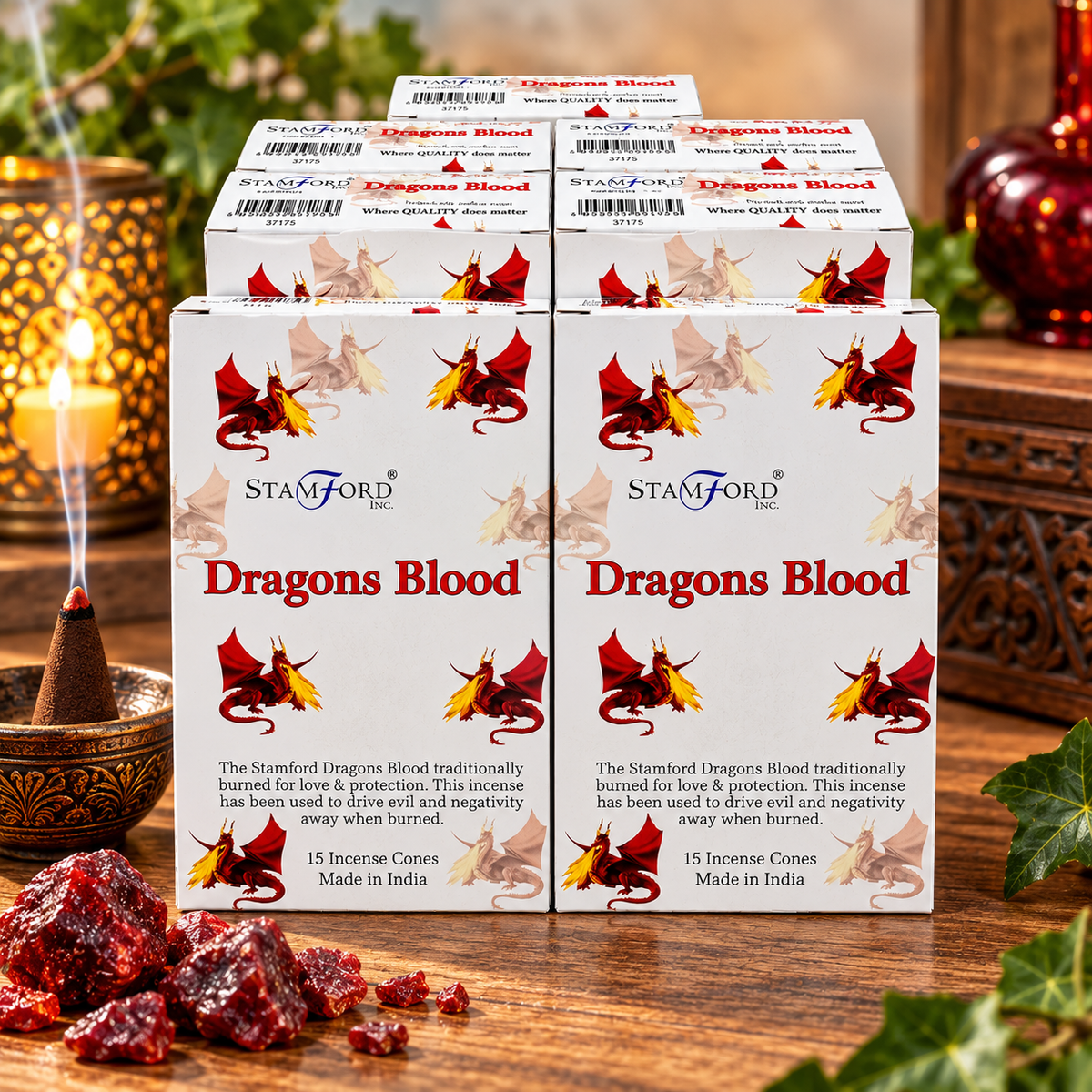 Four boxes of Stamford Inc. 'Dragons Blood' incense cones arranged on a wooden surface, with a burning incense cone and dried red incense leaves in the foreground and a warm, decorated background.