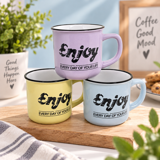 Three enamel-style mugs in pastel purple, yellow, and light blue are stacked on a wooden tray. Each mug has a black rim, black script text reading 'Enjoy', and smaller text 'EVERY DAY OF YOUR LIFE'.