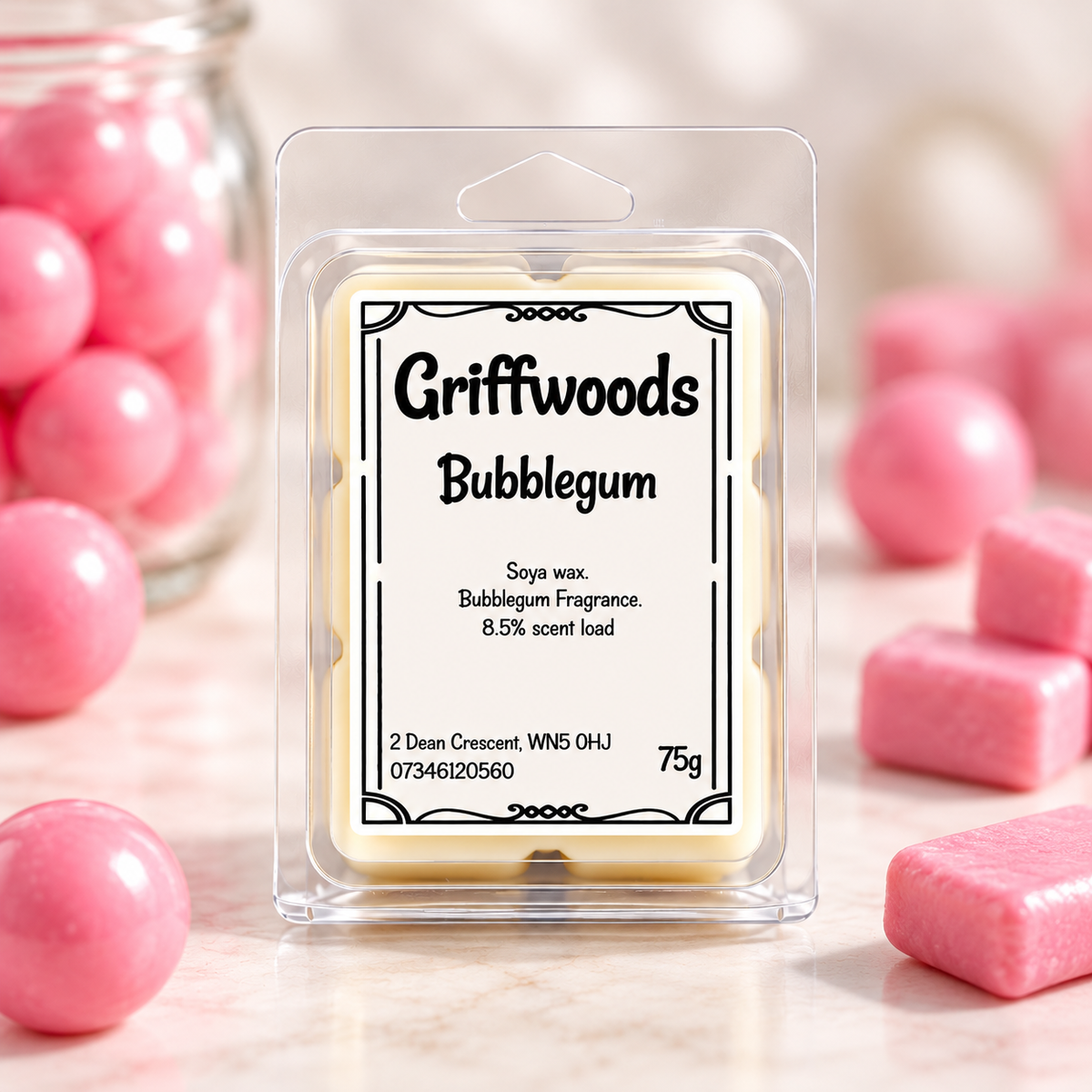 A packaged wax melt labeled 'Griffwoods Bubblegum' in a clear plastic clamshell package, centered on a light marble surface with pink bubblegum candies and pink spheres around it.