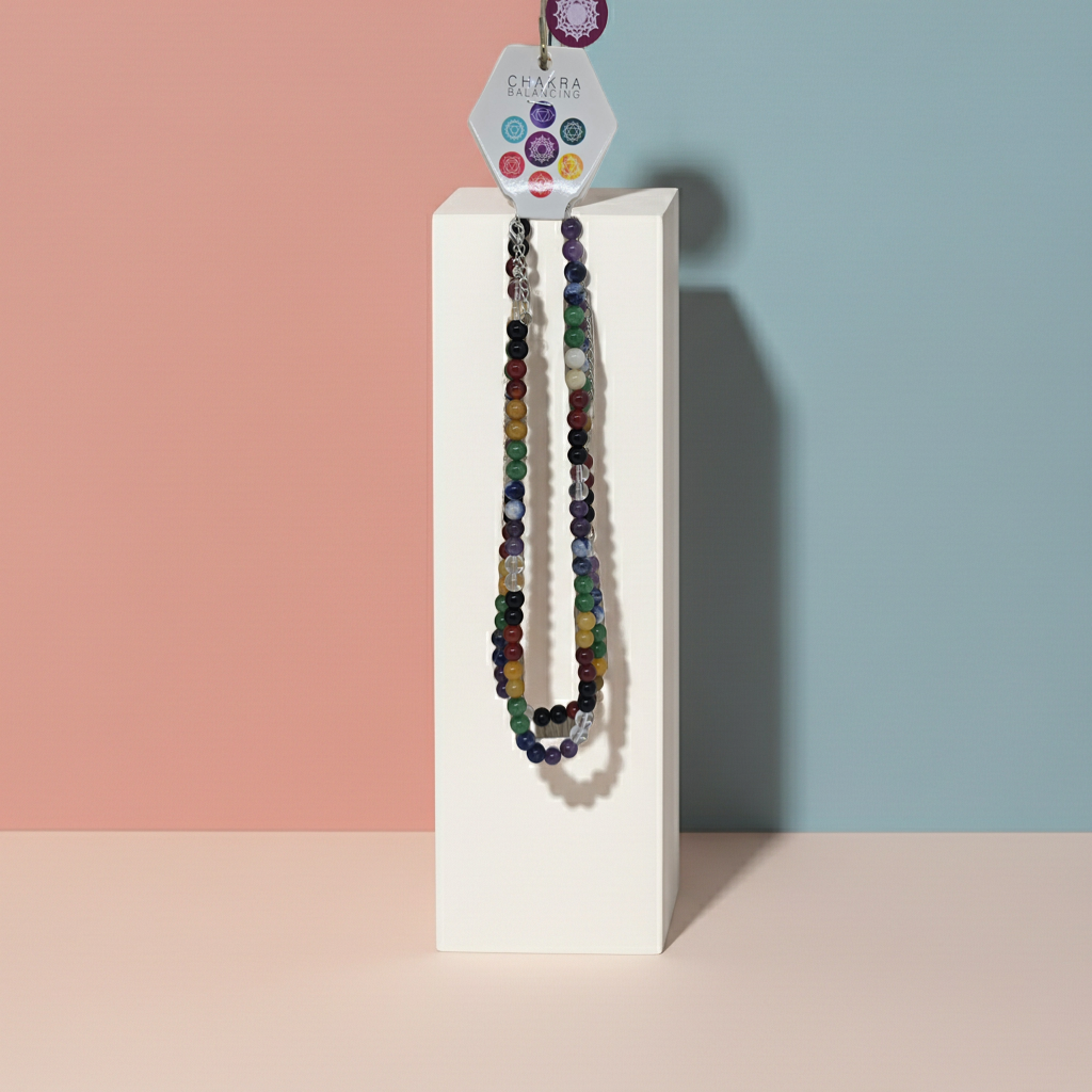 Colourful beaded energy balancing Chakra necklace on a white stand against a pastel background
