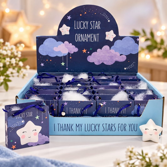 A retail display box and matching small gift bag for a 'Lucky Star Ornament' product. The packaging features a dark blue starry sky design with purple clouds, white stars, and the text 'Lucky Star Ornament' and 'I THANK MY LUCKY STARS FOR YOU'.
