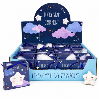 A retail display box and matching small gift bag for a 'Lucky Star Ornament' product. The packaging features a dark blue starry sky design with purple clouds, white stars, and the text 'Lucky Star Ornament' and 'I THANK MY LUCKY STARS FOR YOU'.