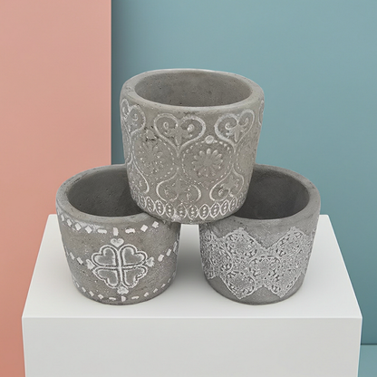 Three decorative concrete Candle Holders with intricate patterns on a white platform against a multicolored background.