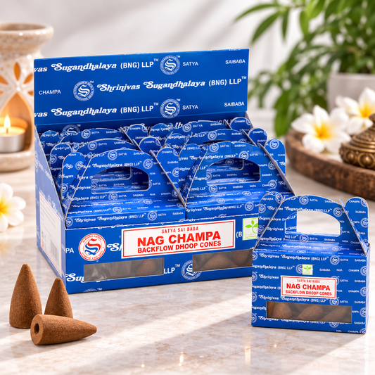 A retail display box and individual box of Nag Champa Backflow Dhoop Cones on a marble surface, with several brown incense cones in front and decorative candles, flowers, and greenery in the background.
