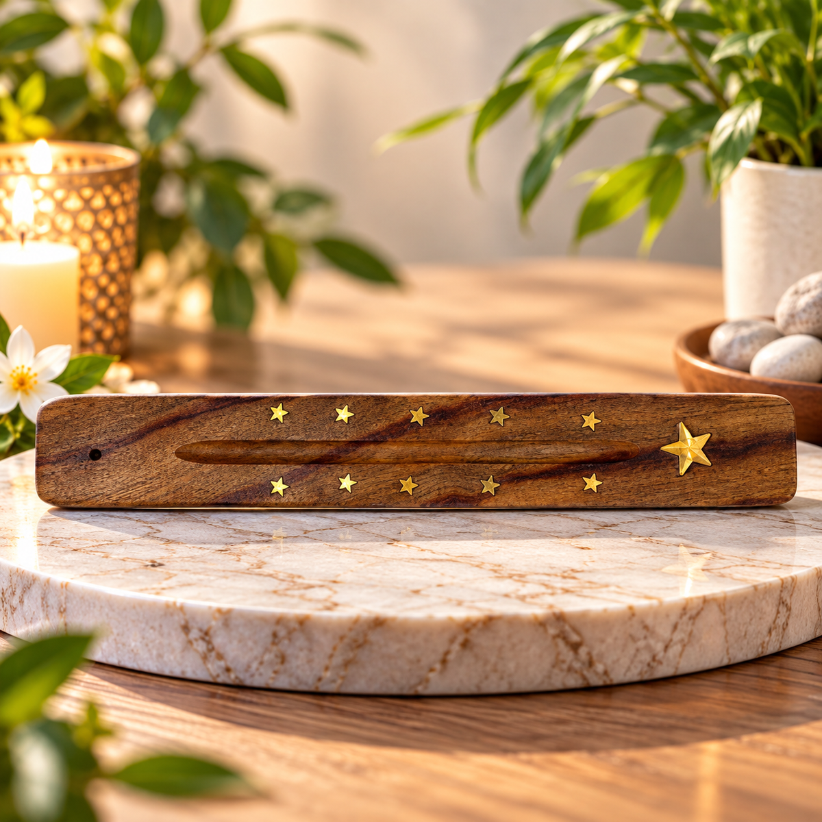 A rectangular wooden incense stick ash catcher with a design of small gold star accents, displayed on a round marble platter in a warm, softly lit setting with plants and candles in the background.