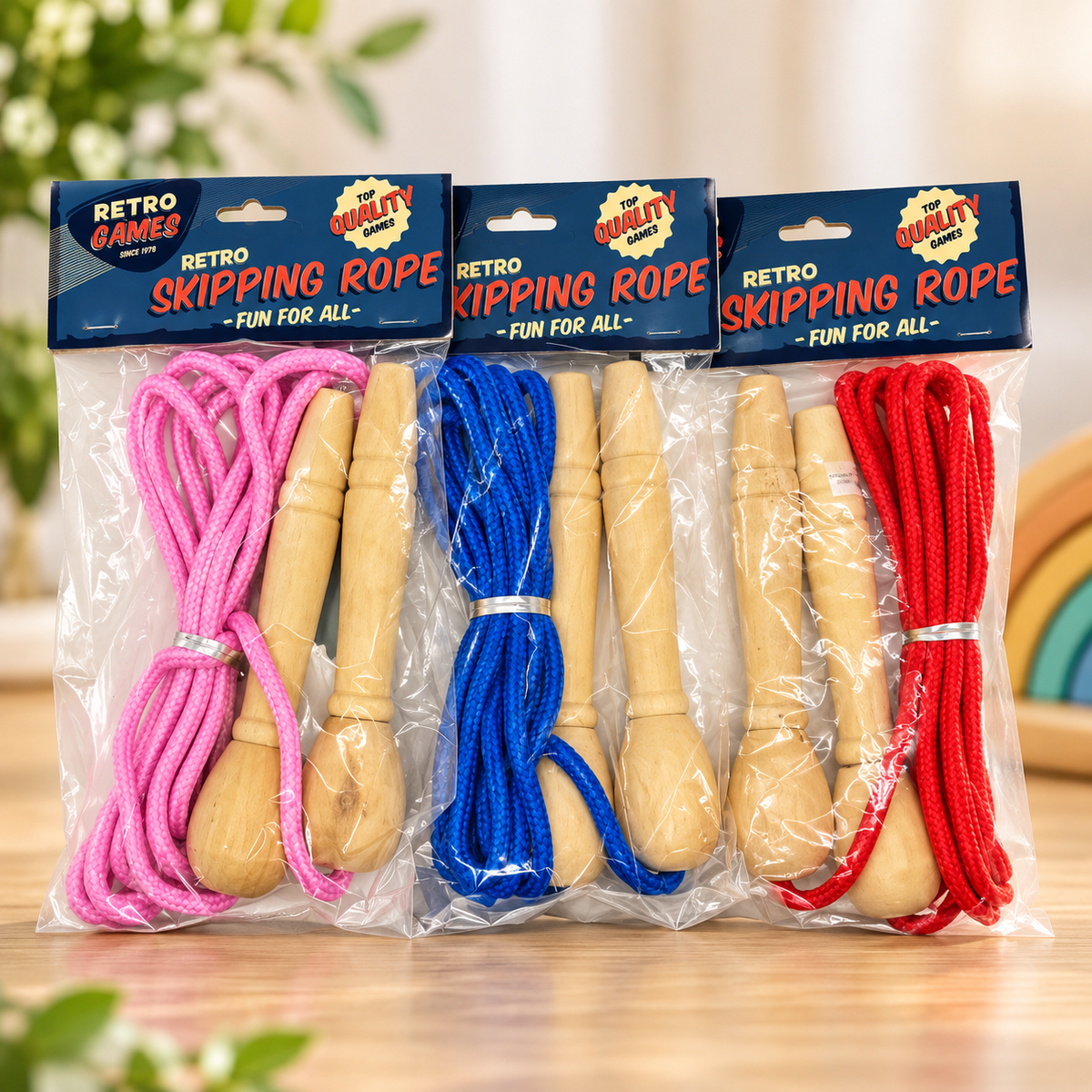Three packaged retro skipping ropes on a tabletop. Each package contains a pink, blue, and red rope with light wooden handles, sealed in clear plastic with blue and red retail headers that read 'Retro Skipping Rope' and 'Fun for All.