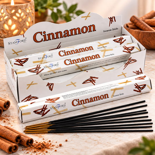 A display of Stamford Cinnamon incense sticks in white boxes with brown and gold branding, with several black incense sticks laid out in front on a light surface, surrounded by cinnamon sticks and warm ambient decor.