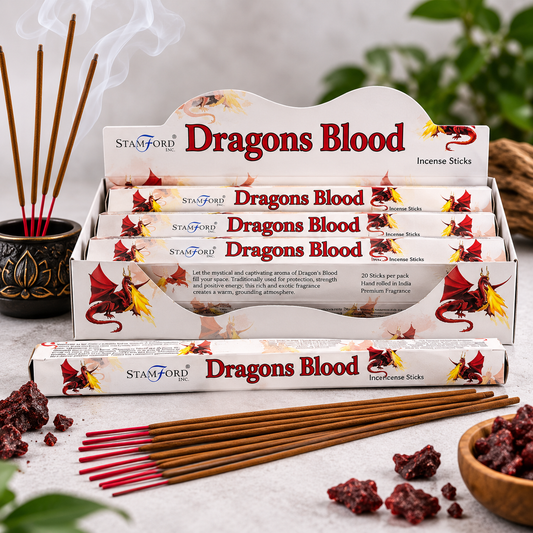 A display of Stamford Dragons Blood incense sticks, with several sticks burning in a black decorative pot on the left and loose incense pieces and a small bowl on the right, set on a light stone surface with soft green foliage in the background.