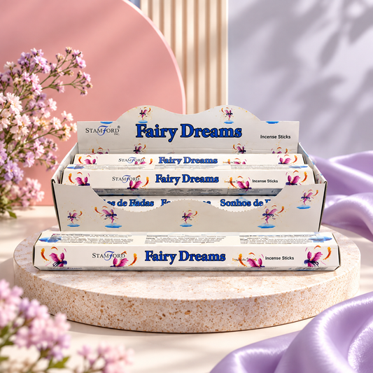 A display box and individual packs of Stanford Fairy Dreams incense sticks, styled on a round stone pedestal with soft pink and purple fabric and small flowers in the background.