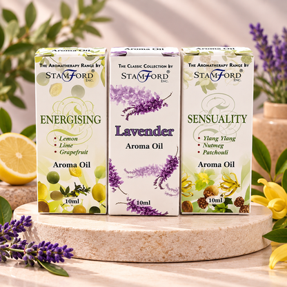 Three boxes of Stamford Aroma Oil arranged on a round stone plinth with flowers and citrus around them. The center box is lavender aroma oil, flanked by energising and sensuality boxes.