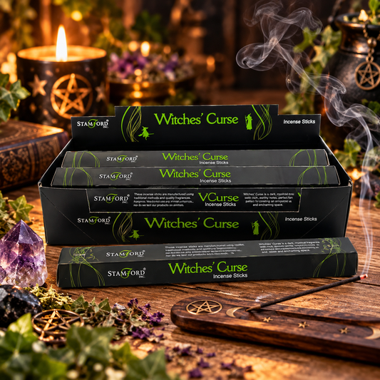 Five boxes of Stamford Witches' Curse incense sticks are stacked in a wooden tray on a rustic wooden table, surrounded by mystical props including a burning candle, a purple crystal, dried herbs, and a wooden wand with a pentagram symbol. Smoke is visibly rising from the incense sticks.
