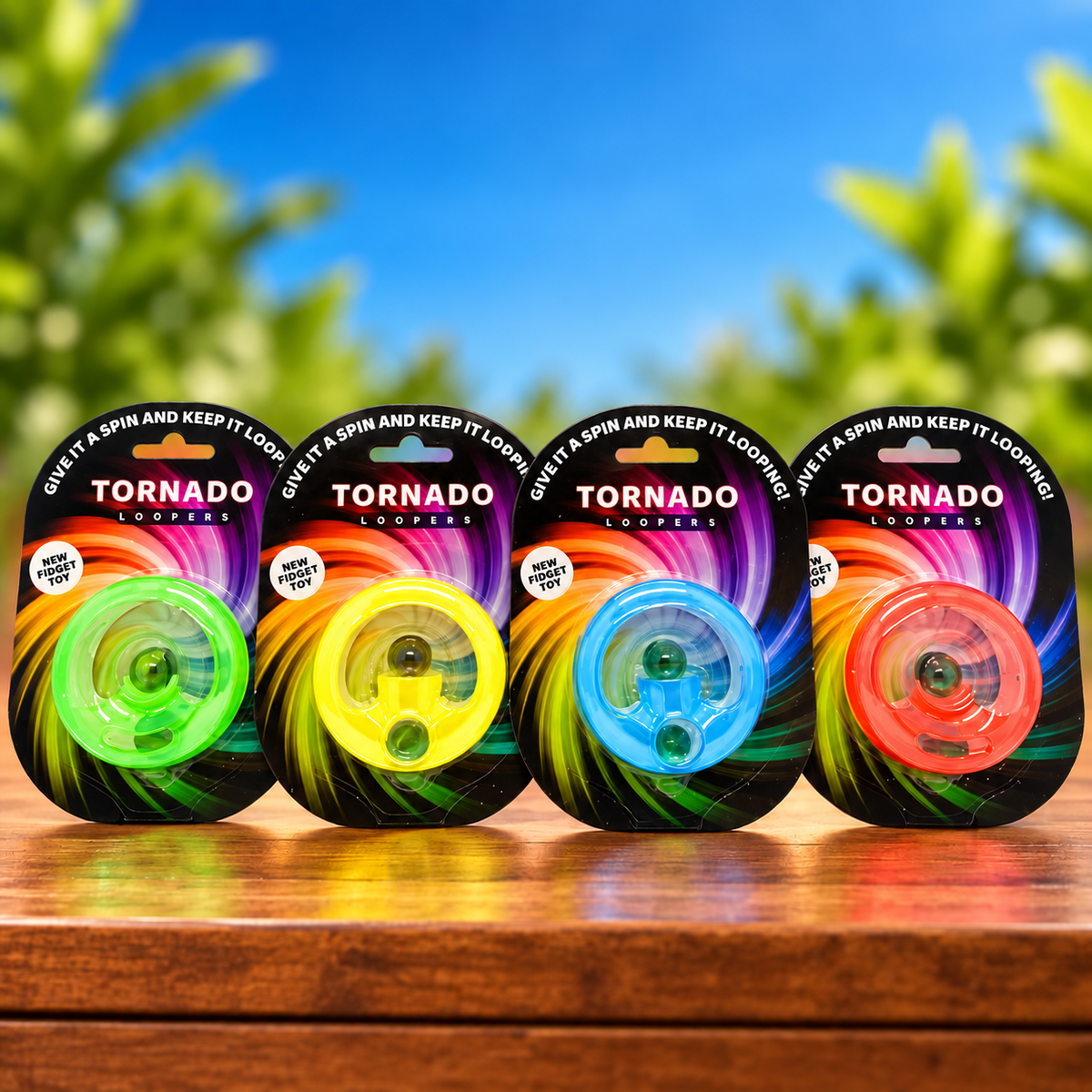 Four packaged Tornado Loopers standing side by side on a wooden surface with a blurred outdoor background of blue sky and green leaves. The packages show different loop colors: green, yellow, blue, and orange.