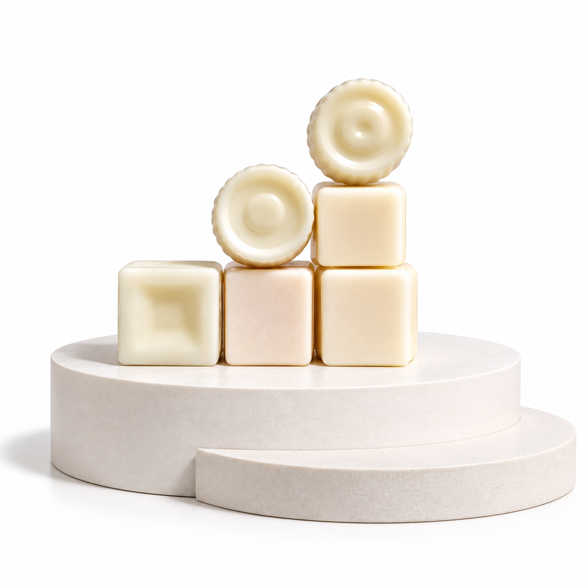 Six pale cream-colored wax melts or soap bars arranged in a small pyramid on a matching round pedestal against a clean white background.