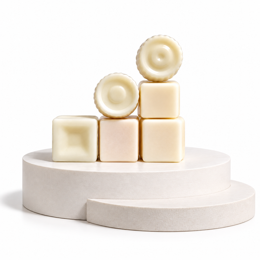 Six pale cream-colored wax melts or soap bars arranged in a small pyramid on a matching round pedestal against a clean white background.