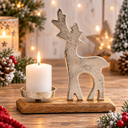 A rustic holiday tabletop scene featuring a silver-toned metal reindeer figurine on a wooden base next to a lit white pillar candle in a metal holder, with warm string lights and Christmas decorations blurred in the background.