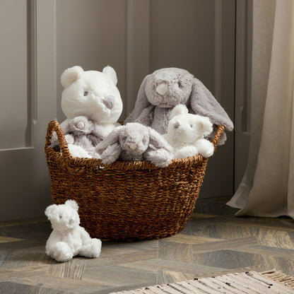 Basket filled with plush toys including a bear, rabbit, and teddy bear on a wooden floor.