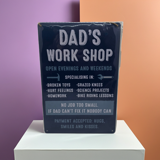 Decorative dark blue sign for 'Dad's Workshop' with humorous text written in white and a lighter blue tone on a white platform against a purple and orange background.